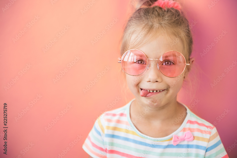 Portrait of crazy little teen girl shows tongue in pink sunglasses