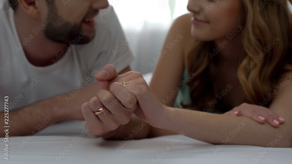 Couple holding hands and lying on bed, relaxing on honeymoon, young family