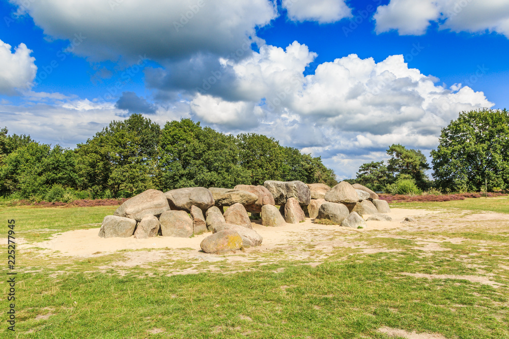 A dolmen, D53,  in the province of Drenthe in the Netherlands with a background of oak trees and a beautiful Dutch cloudy sky. A dolmen is construction work from the new stone age