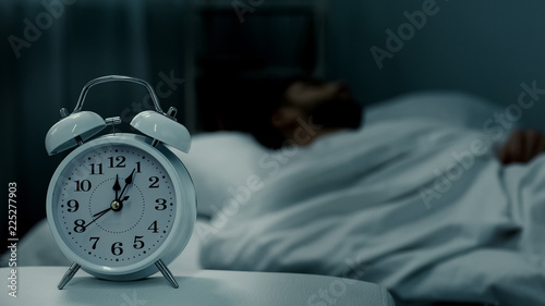 Man sleeping in bed, alarm clock showing midnight, rest hours, healthy sleep photo