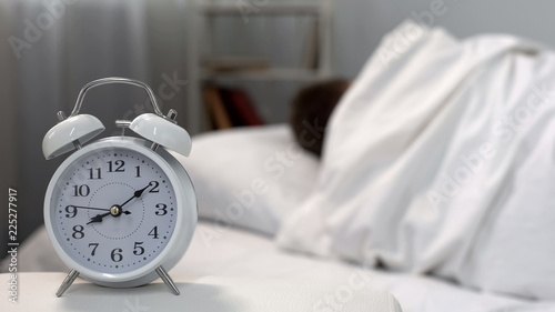Sleeping man ignoring bed clock in morning, time management, self-discipline