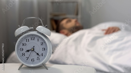 Male oversleeping in morning, alarm ringing at night table, time management