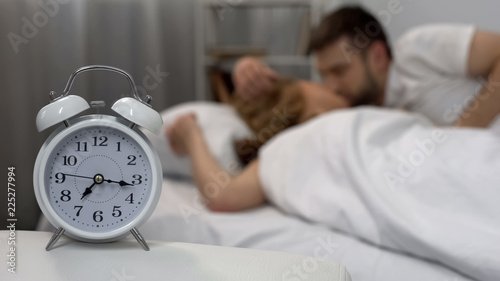 Happy male kissing his girlfriend woken up with alarm clock in morning, family