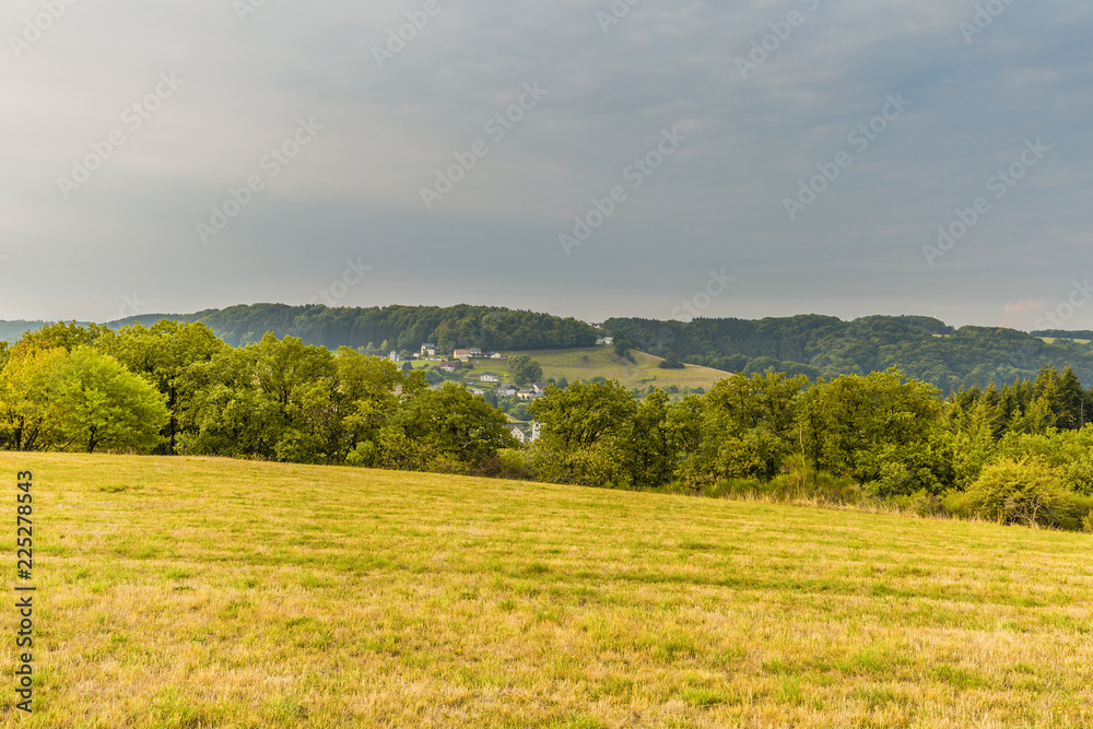 Eifel landscape at sunrise with view on village Udscheid against background with morning fog and hills with forests and sky with light clouds