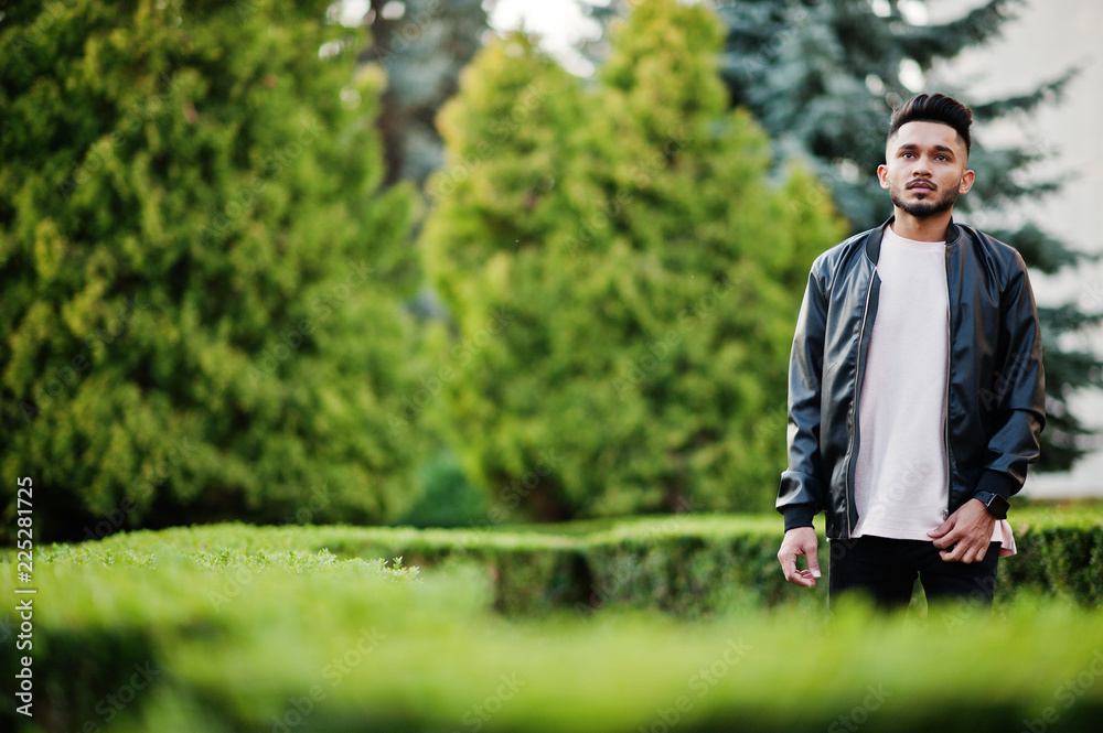 Stylish indian beard man at black leather jacket. India model posed at green garden of city. Stylish indian beard man at black leather jacket. India model posed at green garden of city.