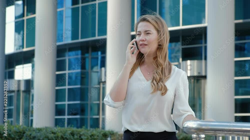 Young business woman talking is using smartphone in city park business center Young business woman talking is using smartphone in city park business center