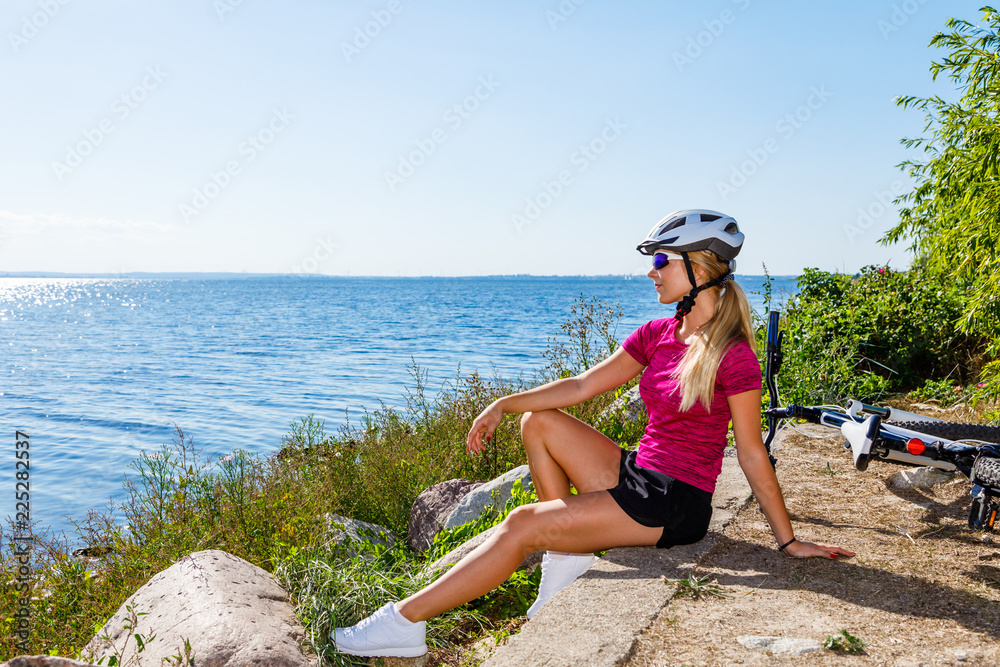 Wunschmotiv: Young woman sitting with bike at seaside #225282537