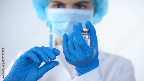 Nurse in mask taking vaccine with syringe from ampoule, epidemic prevention