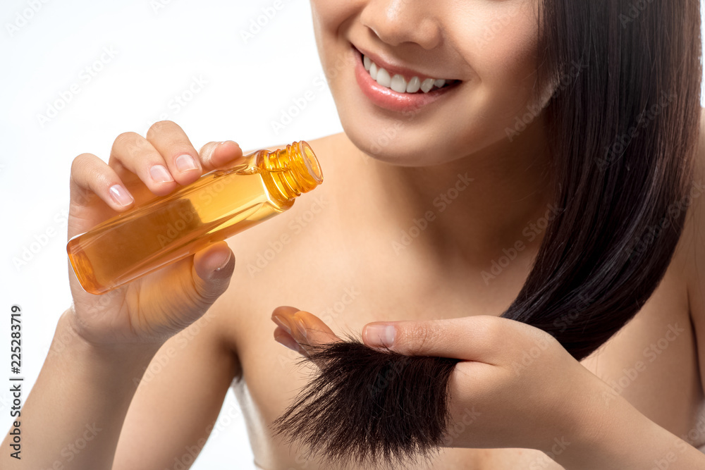 Fototapeta premium cropped shot of smiling woman pouring oil on split ends isolated on white