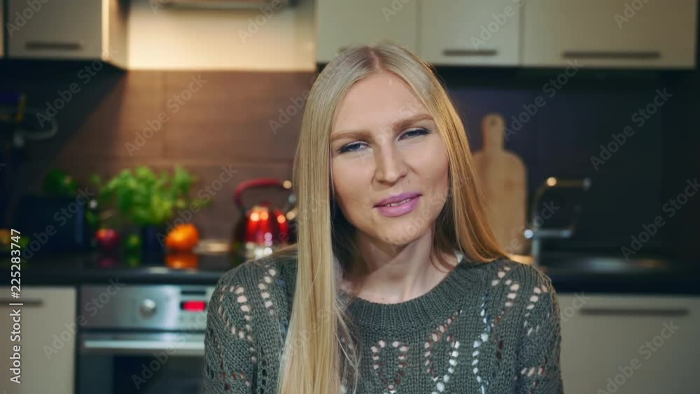Pretty woman smiling and waving hand. Lovely young female smiling and looking at camera while greeting vlog audience by waving hand on background of stylish kitchen. Pretty woman smiling and waving hand. Lovely young female smiling and looking at camera while greeting vlog audience by waving hand on background of stylish kitchen.