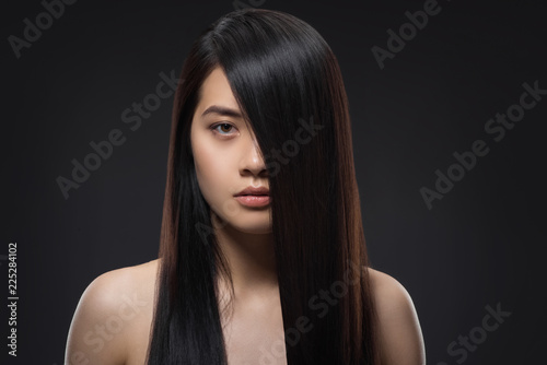 portrait of young asian woman with beautiful and healthy dark hair looking at camera isolated on black
