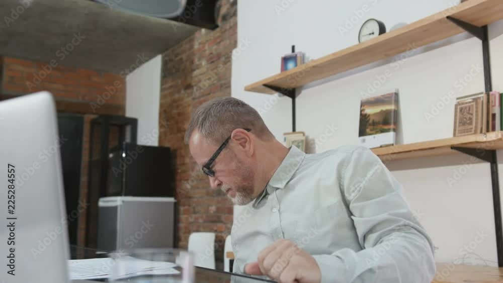 Old Caucasian man in shirt celebrating successful project. Amazing happy man with grey beard wearing sombrero. Victory. Lifestyle. Laptop on table. Indoors. Old Caucasian man in shirt celebrating successful project. Amazing happy man with grey beard wearing sombrero. Victory. Lifestyle. Laptop on table. Indoors.