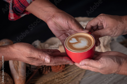 Red cup of cappuccino with latte art coffee serving by hipster man hands, Coffee and breads on wooden table.