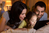 people and family concept - happy mother, father and little daughter with tablet pc computer in bed at night at home
