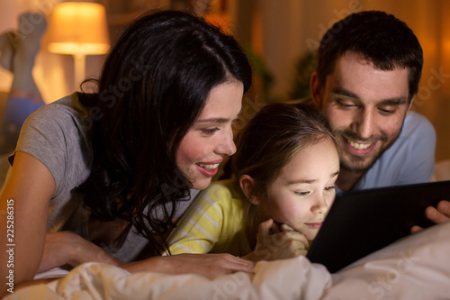 people and family concept - happy mother, father and little daughter with tablet pc computer in bed at night at home