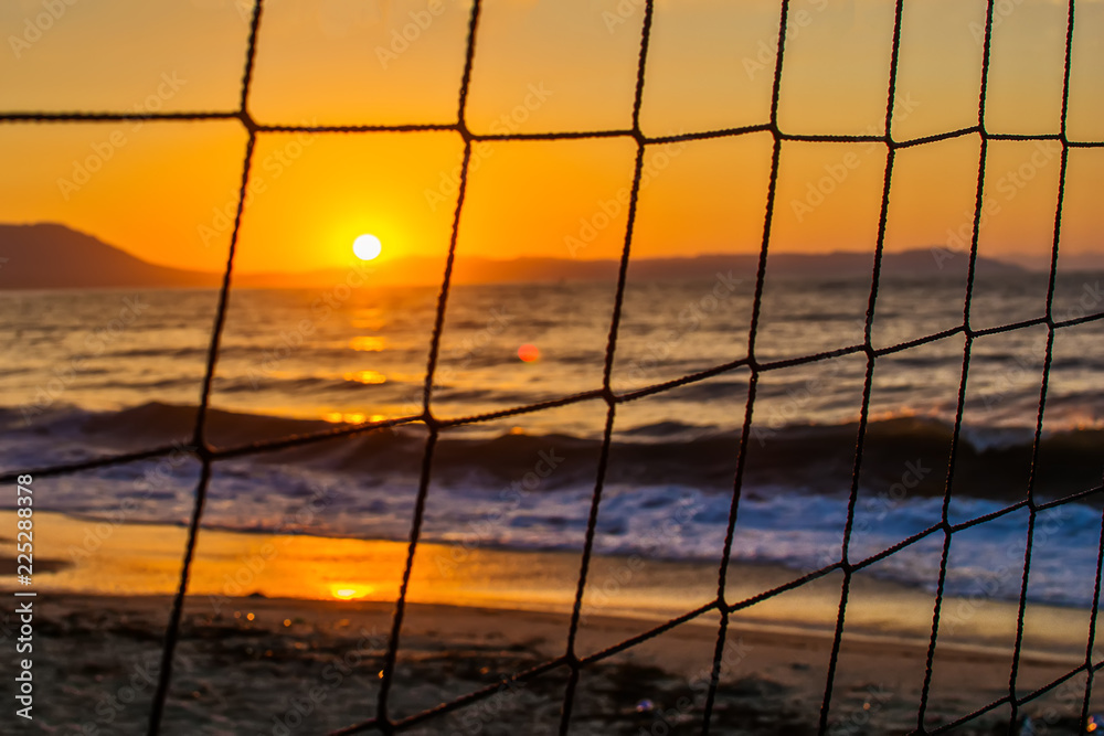 Fototapeta premium View of the sunrise through the volleyball net. Early morning , dramatic sunrise over sea and mountain.