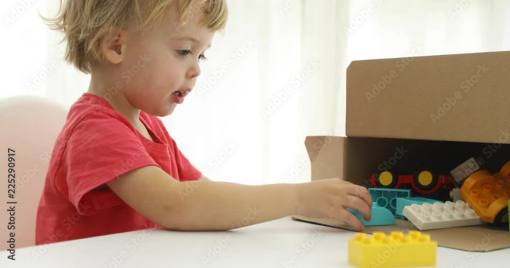 Little boy tidying up his toys cubes from the kit of Bricks in box Little boy tidying up his toys cubes from the kit of Bricks in box