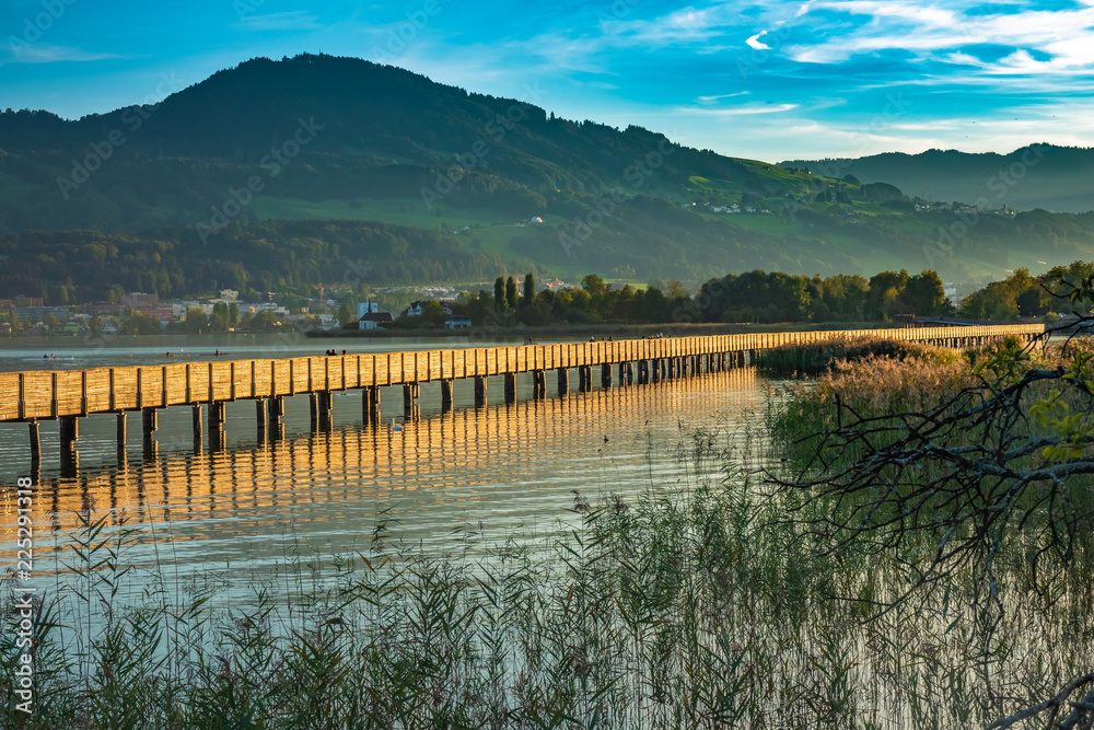 The sunset paints the historical holzsteg pedestrian bridge crossing the Upper Zurich Lake (Obersee) in a honey gold color. Part of the old Way of Saint James, Switzerland