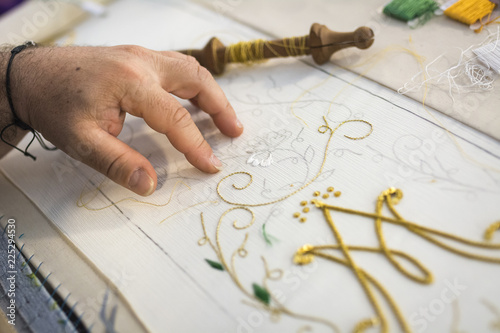 Detail of a man's hands embroiderer with a sewing thread on.Details of embroiderywith gold-colored thread