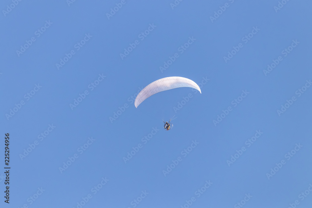 Paraglider flying with a paramotor over clear blue sky Paraglider flying with a paramotor over clear blue sky