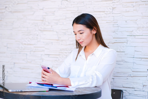 Asian bisiness woman dialing number on cellphone using good internet connection indoors. Kazakh female puzzled on watching video in social networks via cellular while sitting in cafe. photo