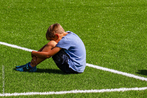 Sad disappointed boy sitting on the grass in stadium photo