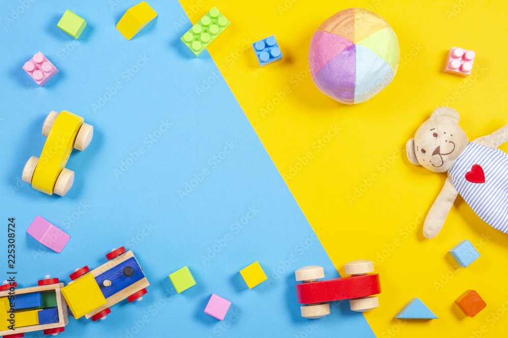 Obraz premium Baby kids toys frame with teddy bear, wooden toy train, car, colorful bricks on blue and yellow background. Top view