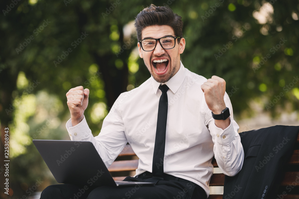 Business man outdoors in the park using laptop computer make winner gesture. Business man outdoors in the park using laptop computer make winner gesture.