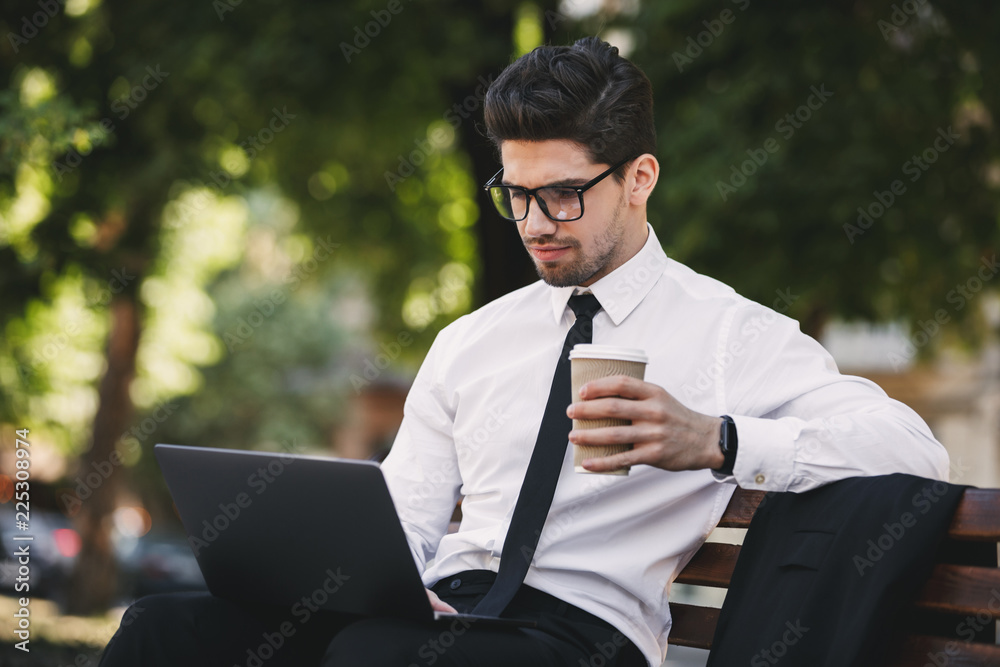 Business man outdoors in the park using laptop computer drinking coffee. Business man outdoors in the park using laptop computer drinking coffee.