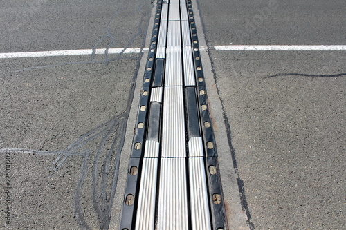 Highly used worn out metal and rubber bridge segments connection surrounded with cracked asphalt and white line on warm sunny day