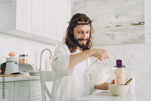 happy Jesus pouring milk into bowl with corn flakes on breakfast in kitchen at home
