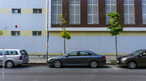 cars parked on the road against a background of a new urban building. a street urban landscape without people, just cars and a building. © Ivan