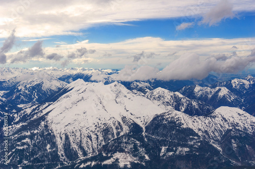 Blick auf gewaltige schneebedeckte Berge umgeben von dramatischen Wolken vor blauem Himmel.