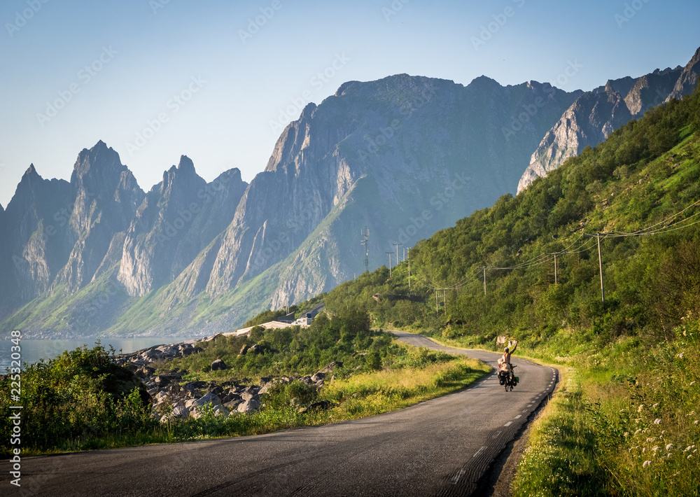 A boy is travelling by bike with his dog in Lofoten Islands (Norway). Landscape on the background with mountain silhouette
