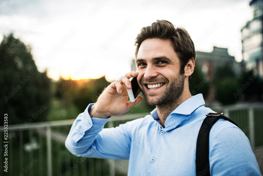 A young businessman with a smartphone walking on a bridge at sunset. A young businessman with a smartphone walking on a bridge at sunset.
