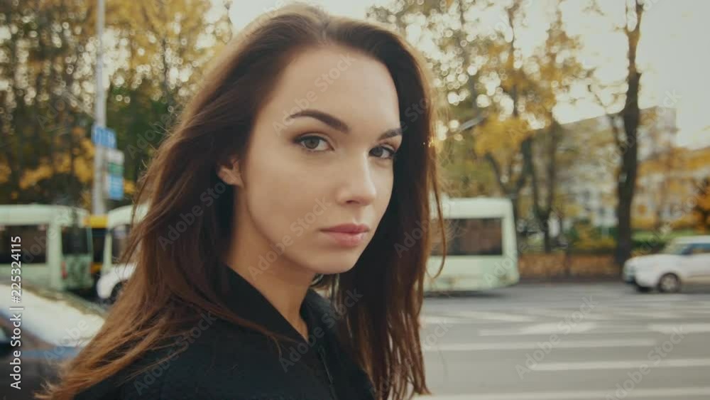 Beautiful girl walking in autumn street. Close up portrait of young woman looking at camera. Pretty model walking in slow motion at autumn city Beautiful girl walking in autumn street. Close up portrait of young woman looking at camera. Pretty model walking in slow motion at autumn city