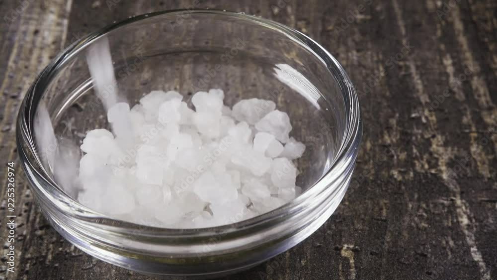 Slow motion crystals of coarse sea salt pour into a glass bowl close up Slow motion crystals of coarse sea salt pour into a glass bowl close up