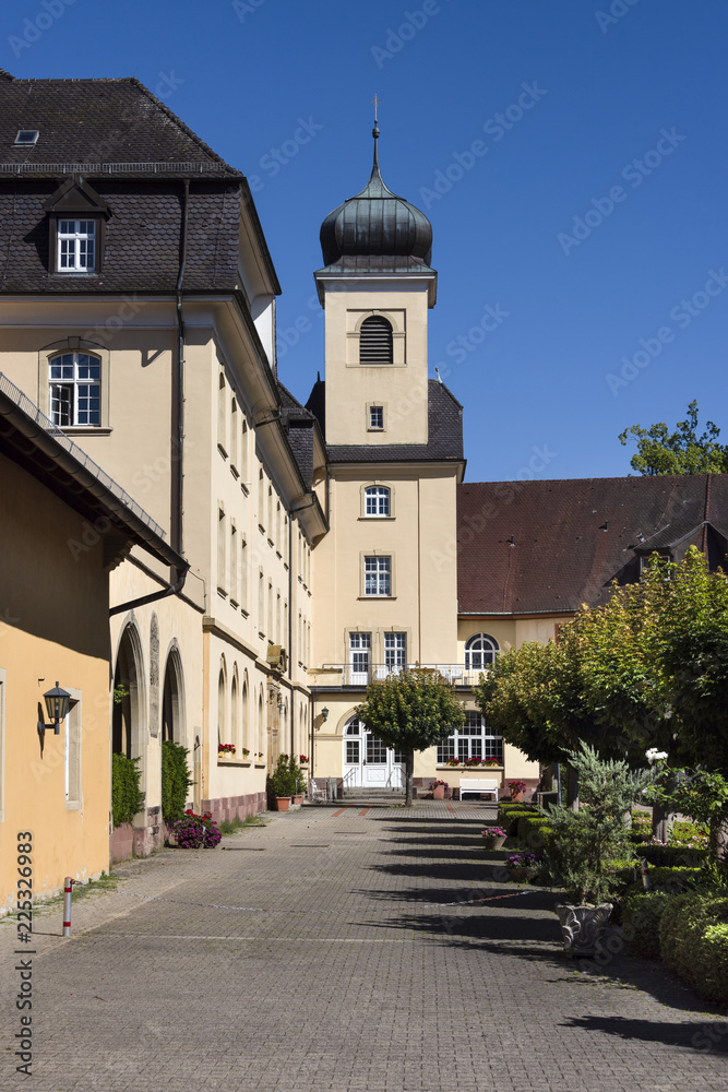 Germany, Baden-Wuerttemberg, Heitersheim: View of famous Maltese castle in the center of the German small town with monastery, public park, tower, green trees, grass and blue sky in background.
