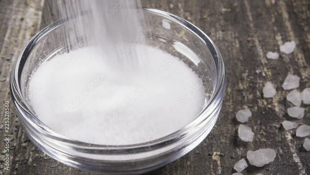 Slow motion small table salt pour into a glass bowl close up Slow motion small table salt pour into a glass bowl close up