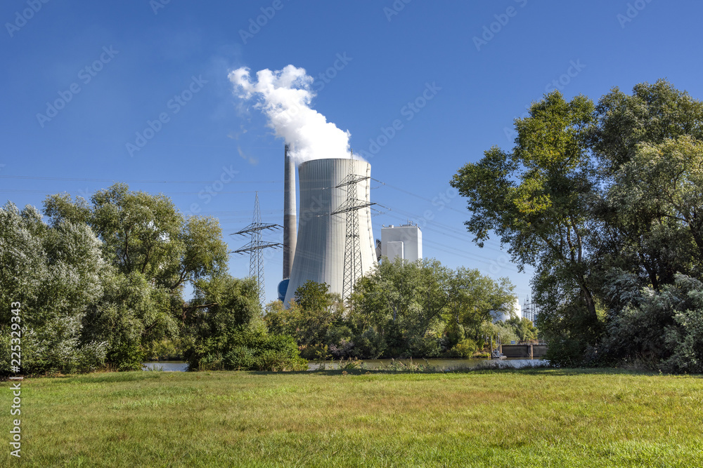Big power plant with white exhaust gases steam, green trees, grass field, skyline and blue sky in background - concept electricity power business technology consumption nature environmental pollution Big power plant with white exhaust gases steam, green trees, grass field, skyline and blue sky in background - concept electricity power business technology consumption nature environmental pollution