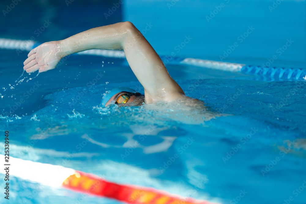 Side view of young sports man in blue cap floating on path in pool