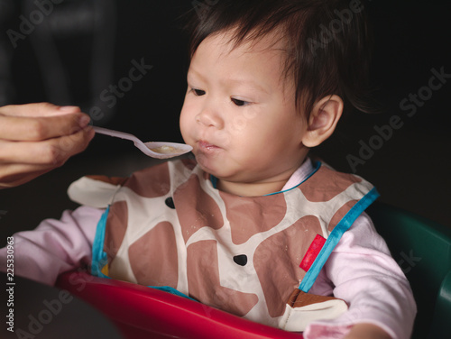 Wallpaper Mural Asian toddler with dirty bib eat meal  by mom feed. Torontodigital.ca
