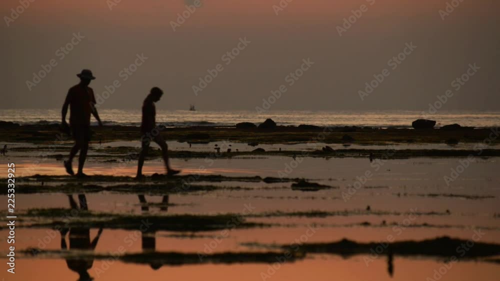 Family with four people walking on sea floor during low tide after sunset Family with four people walking on sea floor during low tide after sunset