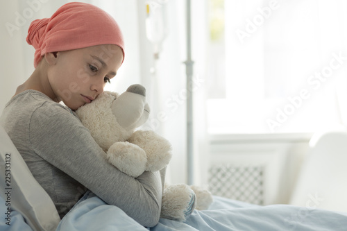 Weak girl with cancer wearing pink headscarf and hugging teddy bear photo