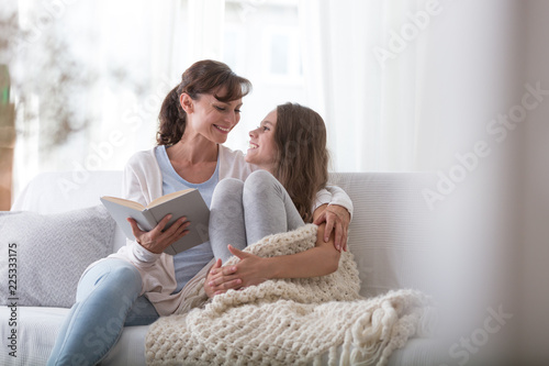 Happy mother reading book to smiling daughter while relaxing at home