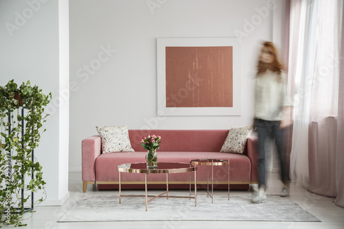 Blurred woman walking in a feminine living room interior with a sofa, coffee table and painting