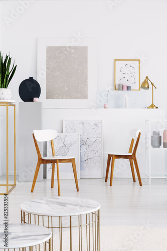 Two white wooden chairs  and tables with marble counter tops in white living room with maps and and art on the wall