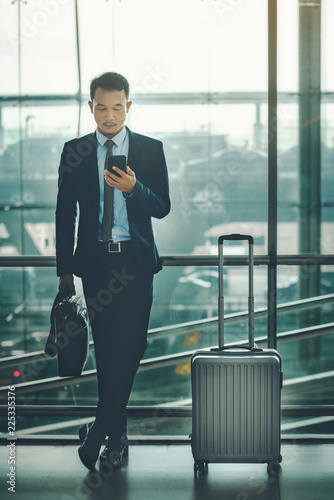 An Asian businessman is using a smartphone to get in business while waiting for a trip in the airport.