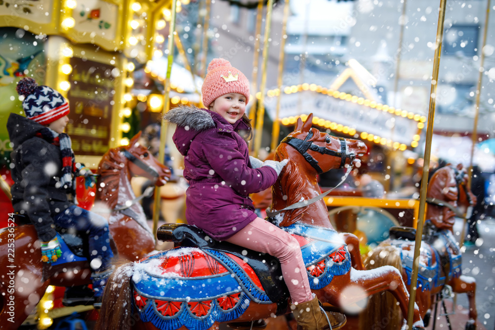 Obraz premium Adorable little kid girl riding on a carousel horse at Christmas funfair or market, outdoors.