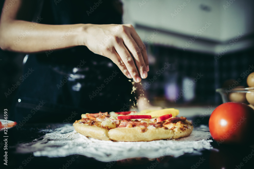 Close up of woman hand putting oregano over tomato and mozzarella on a pizza. Cooking concept